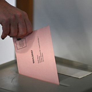 Frau gibt Briefwahlstimme in eine Wahlurne.