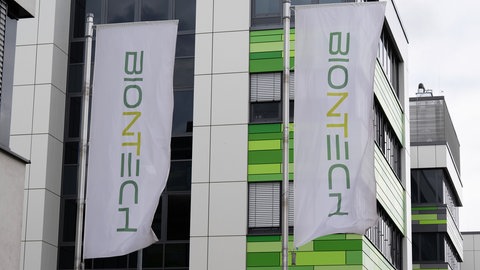 Fahnen wehen vor der Firmenzentrale des Impfstoffherstellers Biontech. Das Unternehmen plant einen massiven Stellenabbau und die Schließung mehrerer Produktionsstandorte. Bei der Hauptversammlung wird es spannend.