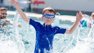 Ein Kind spielt im Freibad mit dem Wasser.