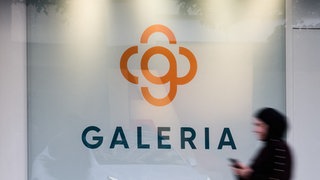 Eine Frau geht am Logo an einer Galeria Filiale entlang.