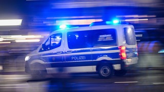 Ein Mannschaftswagen der Polizei fährt mit Blaulicht durch die Nacht.