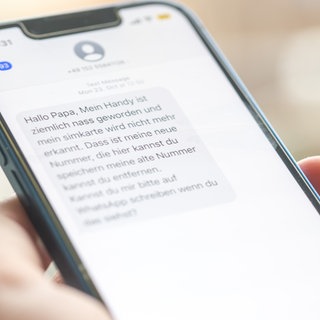 Eine Frau hält ein Smartphone in ihrer Hand, auf dessen Display eine Betrugs-SMS zu lesen ist.