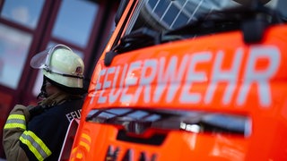Ein Feuerwehrmann steht bei einem Einsatz vor einem Löschfahrzeug (Symbolbild).