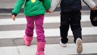 Zwei Kindergartenkinder gehen Hand in Hand über einen Zebrastreifen.