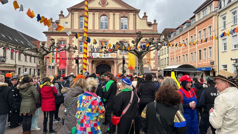 Menschen in Fastnachtskostümen stehen vor dem Rathaus in Rastatt.