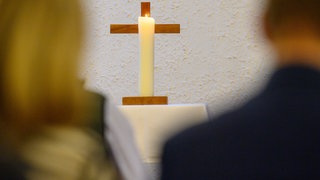 Eine Kerze brennt vor einem Kreuz. 