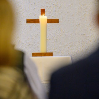 Eine Kerze brennt vor einem Kreuz. 