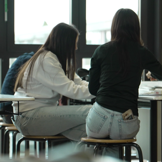 Schüler mit Handys während sie an Schultischen sitzen. (Archivbild)