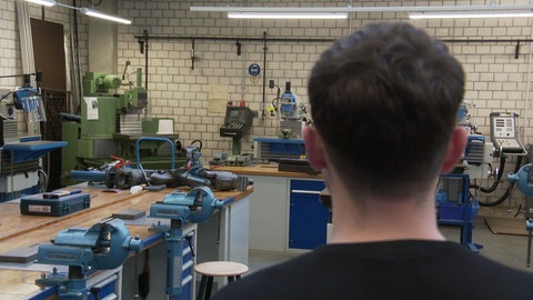 Ein junger Mann von hinten fotografiert in einer Werkstatt an einer Berufsschule.