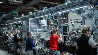 Frauen stehen bei einem Automobilzulieferer an einem Band und arbeiten.