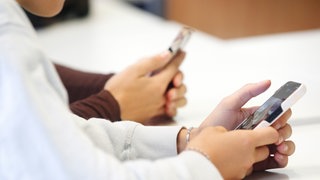 Zwei Schülerinnen benutzen das Handy während des Unterrichts.