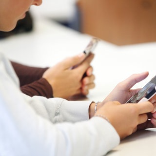 Zwei Schülerinnen benutzen das Handy während des Unterrichts.