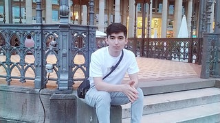 Sonatullah Uzbek sitzt auf eier Treppe in einem kleinen Park