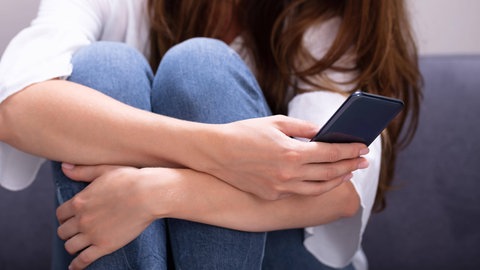 Eine Frau sitzt auf dem Sofa und benutzt ihr Smartphone.