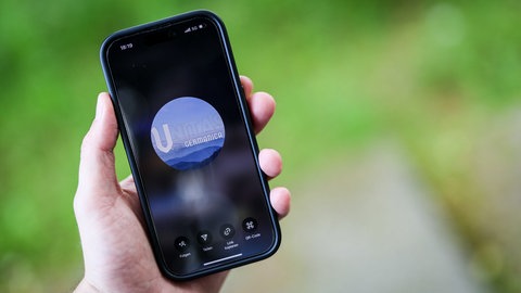 Ein Mann hält ein Smartphone in der Hand, auf der die Instragram-Seite und das Logo von "Unitas Germanica" zu sehen ist.