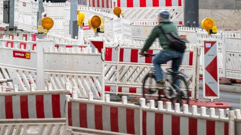 Symbolbild | Ein Fahrradfahrer fährt über eine Strasse, die mit Warnbaken vollgestellt ist.