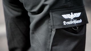 Ein Mann trägt eine schwarze Cargo-Hose, auf deren Tasche ein Reichsadler und der Schriftzug Deutschland aufgedruckt sind (Symbolbild).