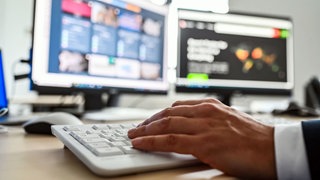 Eine Hand an einer Cimputertastatur vor zwei Bildschirmen. Vor allem Arbeit im Büro ist Teil von einer Ausbildung im Amt.