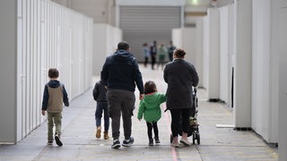 Eine Flüchtlingsfamilie geht durch eine zur Massenunterkunft umfunktionierte Halle. 