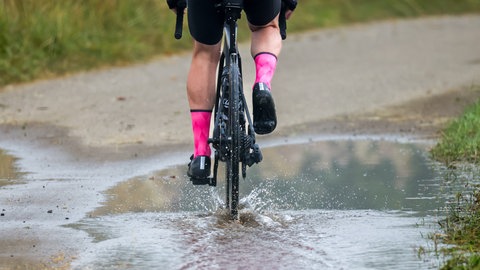 Neue Woche bringt Regen: Ein Mann fährt mit seinem Rennrad durch eine Pfütze. (Archiv)