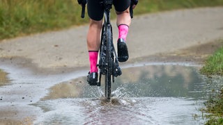 Neue Woche bringt Regen: Ein Mann fährt mit seinem Rennrad durch eine Pfütze. (Archiv)