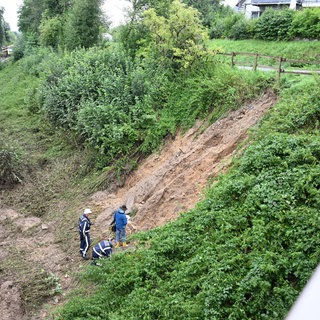 Erde liegt nach einem Hangrutsch auf den Gleisen, im Hintergrund ist der entgleiste Regionalexpress auf der Strecke zu sehen. Bei dem Zugunglück im Südosten Baden-Württembergs sind drei Menschen ums Leben gekommen. 