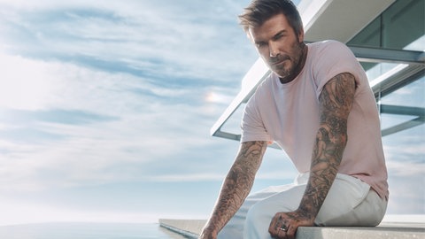 David Beckham sitzt in einem Shirt von Hugo Boss an einem Pool.