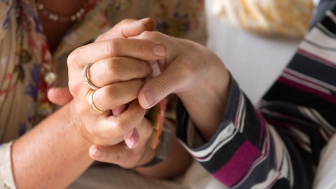 Eine Therapeutin hält im Hospiz St. Martin in Stuttgart die Hand einer todkranken Bewohnerin (Archivbild). Krankenkassen zahlen in diesem Jahr mehr Geld an ambulante Hospize in BW.