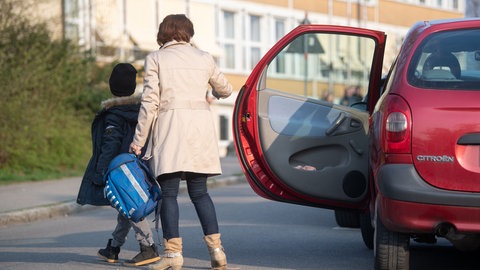 Eine Mama bringt ihr Kind mit dem Auto zur Schule.