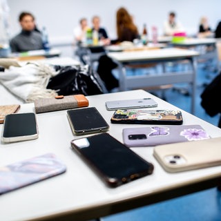 Zahlreiche Smartphones von Schülerinnen und Schülern liegen vor Beginn von schriftlichen Abiturprüfungen auf einem Tisch