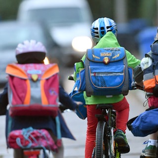 Kinder sind auf einer Straße mit dem Fahrrad unterwegs zur Schule.