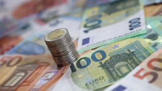 Symbolbild: Ein Stapel mit Zwei-Euro-Münzen steht auf verschiedenen Euro-Banknoten.