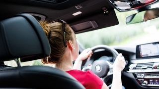 Eine Frau sitzt am Steuer eines Autos. Um einen Führerschein zu bekommen, müssen die Menschen immer mehr Geld bezahlen. Die Politik will gegen die Preis-Steigerungen angehen. Doch oft hängen die hohen Kosten mit den Prüflingen zusammen, die mehr Fahrstunden brauchen und häufiger durchfallen.