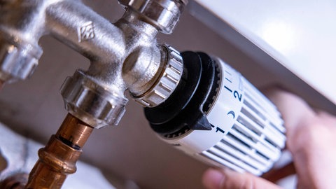 Eine Person dreht am Thermostat einer Heizung.