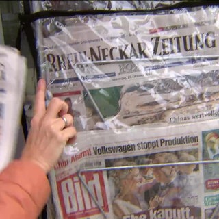 Eine Frau holt eine Rhein-Neckar-Zeitung aus einem Zeitungsständer