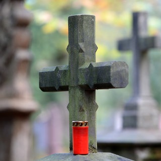 Ein Grablicht steht auf dem Alten Friedhof vor einem Steinkreuz.