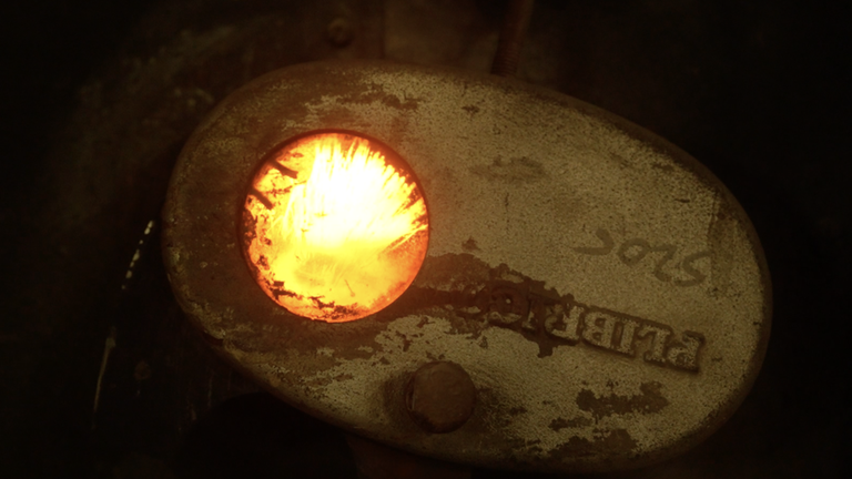 Hinter einem kleinen Bullauge lodern die Flammen im Brennofen.