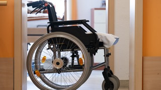 Ein Rollstuhl steht in einem Altenheim vor einem Zimmer. Der Eigenanteil für Pflegebedürftige ist angestiegen. Bewohner und Angehörige belasten die hohen Kosten.