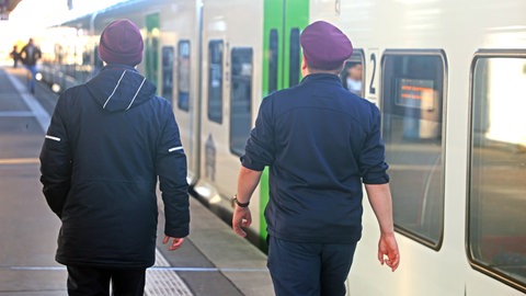 Zwei Zugblegiter laufen im Dienst einen Bahnsteig entlang. Das Land möchte in einem Pilotprojekt Doppelbesetzungen in den Zügen testen. 