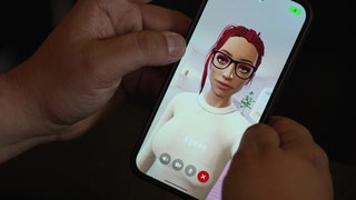 Auf einem Handy-Display ist eine virtuelle Frau mit roten Haaren in einem weißen Oberteil zu sehen.