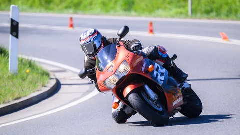 Ein Motorradfahrer fährt in Schräglage auf einem orangenen Motorrad über eine Landstraße im Landkreis Hildesheim.