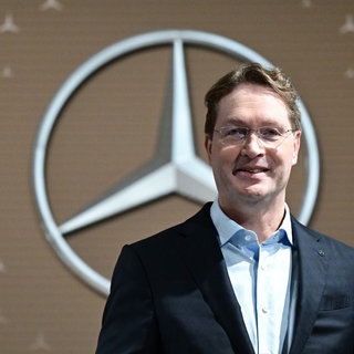 Ola Källenius, Vorstandsvorsitzender der Mercedes-Benz Group AG, steht vor der Bilanz-Pressekonferenz vor einem Mercedes-Benz Markenlogo.