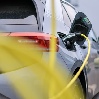 Ein graues E-Auto ist mit einem gelben Kabel zum Aufladen an eine Ladesäule angeschlossen. Durch hohe Verkaufszahlen und bessere Batterien werden gebrauchte Elektroautos immer attraktiver.