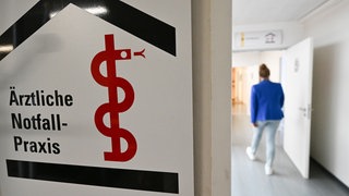 Eine Frau, die nur verschwommen im Hintergrund zu sehen ist, betritt eine Ärztliche Notfall-Praxis.