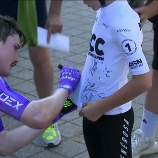 Ein Radsportler unterschreibt auf dem Rad-Trikot eines jungen Fans