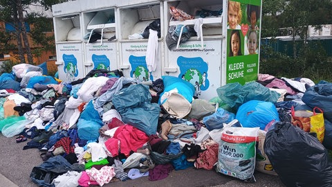 Mülltüten und weggeworfene Klamotten stapeln sich vor überfüllten Altkleidercontainern. Städte haben mit immer mehr wildem Müll zu kämpfen. (Symbolbild)