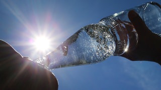 Eine Frau trinkt im Sonnenschein aus einer Perlenflasche sprudelndes Mineralwasser.