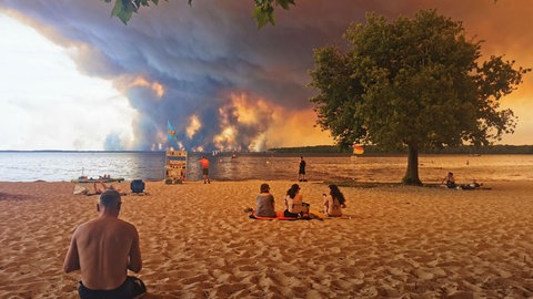 Strandbesuchende sitzen am Strand von Moutchic in Lacanau. Im Hintergrund sind Rauchwolken von den Waldbränden.