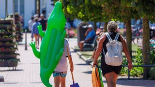 Mit einem aufgeblasenen Krokodil gehen Urlauber über die Strandpromenade. Urlaub ist für viele Menschen Luxus.