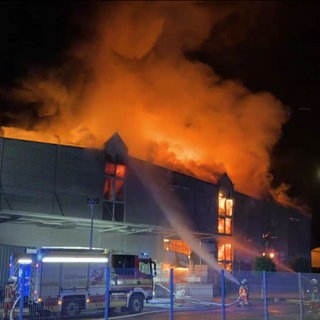 Ein Gebäude eines Textilbetriebs steht in Flammen mit Feuerwehr davor